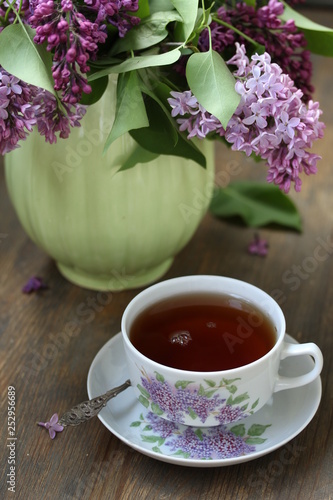 Tea and a bouquet of lilac. Tea in a beautiful cup and a bouquet of lilac in a vase. A spring tea-party. Soft focus
