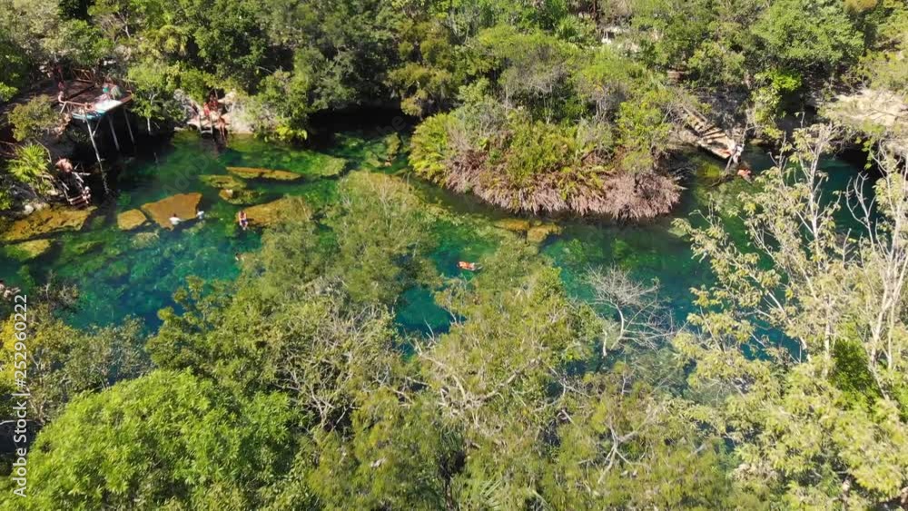 An overhead shot of the jungle and the El Jardin del Eden cenote filled with swimmers. An overhead shot of the jungle and the El Jardin del Eden cenote filled with swimmers.