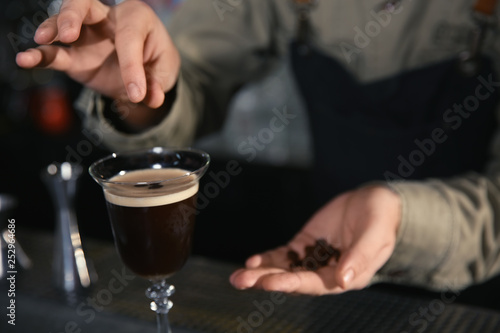 Barman adding coffee bean to martini espresso cocktail at counter, closeup. Space for text