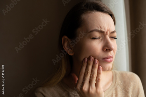 Toothache, and dentistry. Beautiful young woman suffers from terrible severe pain in her teeth, touching her cheek with her hand. Toothache in a woman. Dental care and health concept, dark background