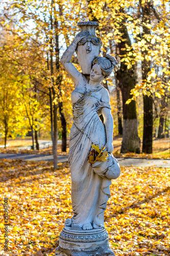 Park sculpture of a woman in antique style with jugs and among autumn foliage. Park Belkino