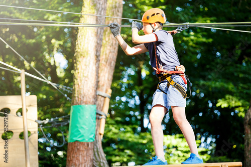 Cute young boy in helmet with climbing equipment in the rope amusement park. Summer camp, holidays concept 
