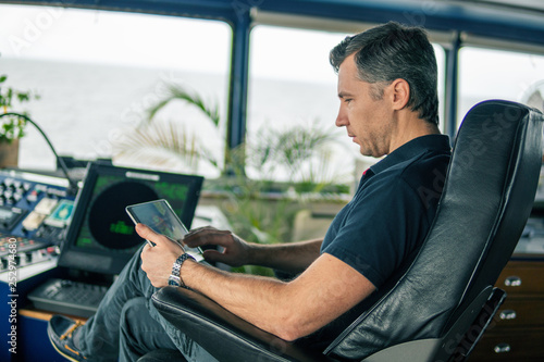 Marine chief officer or captain on navigation bridge watching digital tablet. Internet and home connection at sea.