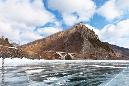 Lake Baikal in early spring. View from the beautiful ice with cracks on the Circum-Baikal Railway - a popular tourist attraction. Stone arch bridge and viaduct over the river Shabartuy