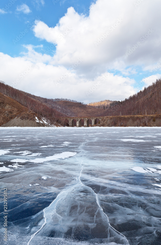 Fototapeta premium Lake Baikal in winter. View from the beautiful ice with cracks on the Circum-Baikal Railway and the stone arched bridge across the River Bolshaya Krutaya Guba