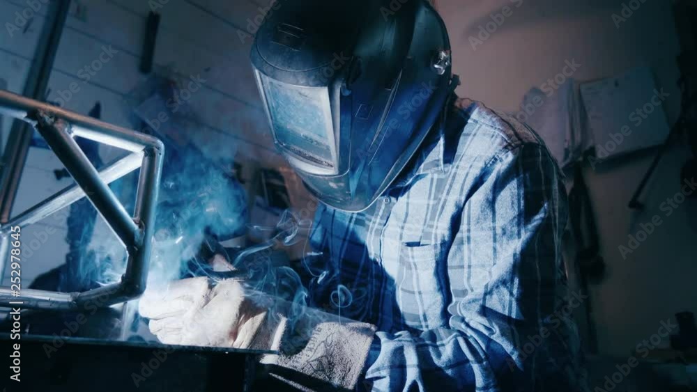 SLOW MOTION INDUSTRIAL WORK SPARKS SMOKE Working man welds metal close up. Welding mask illuminated blue sparks and smoke. Blue smoke curls below glowing reflection in welding mask SLOW MOTION INDUSTRIAL WORK SPARKS SMOKE Working man welds metal close up. Welding mask illuminated blue sparks and smoke. Blue smoke curls below glowing reflection in welding mask