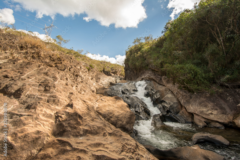 Stony creek in rural Brazil, with lush vegetation around it, on a bright sunny day.