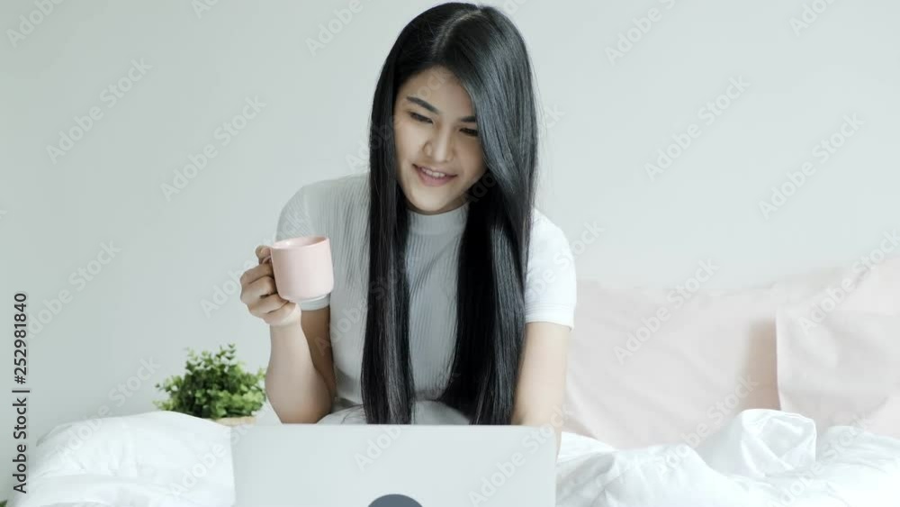 Young beautiful asian woman sitting in bed using laptop and holding coffee cup. Young woman relaxation lifestyle concept. Young beautiful asian woman sitting in bed using laptop and holding coffee cup. Young woman relaxation lifestyle concept.