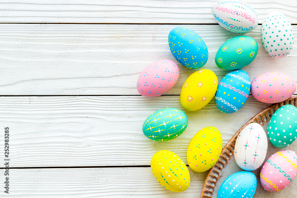Easter traditions. Colorful Easter eggs in basket on white wooden background top view space for text Easter traditions. Colorful Easter eggs in basket on white wooden background top view space for text