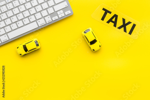 Taxi operator concept. Order taxi online. Sign ner car toy and keyboard on yellow background top view copy space