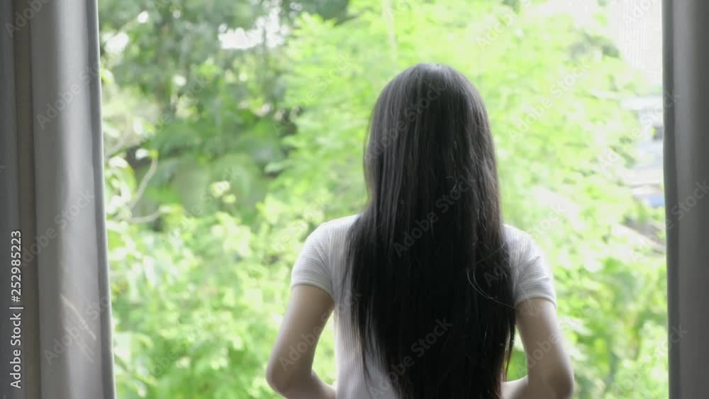 Young beautiful asian woman open bedroom curtain to see green trees background. Relaxing home concept. Young beautiful asian woman open bedroom curtain to see green trees background. Relaxing home concept.