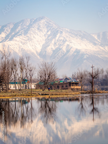 A wooden houseboat on the banks of the Dal Lake with snow covered Zabarwan Hills in the background in Srinagar, Kashmir photo