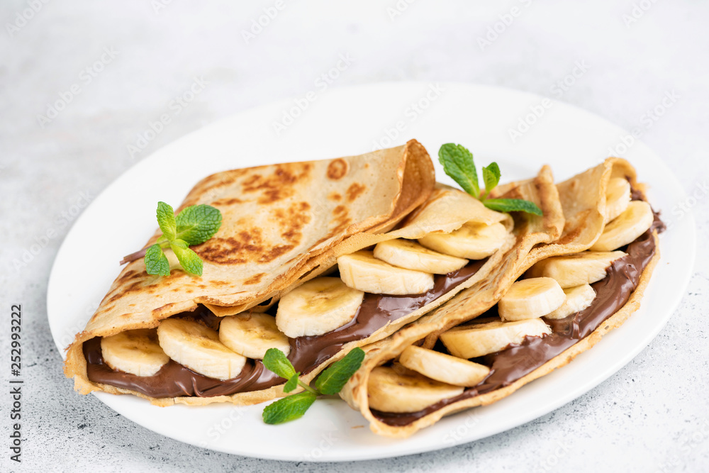 Chocolate hazelnut spread and banana filled crepes on white plate. Isolated. Closeup view