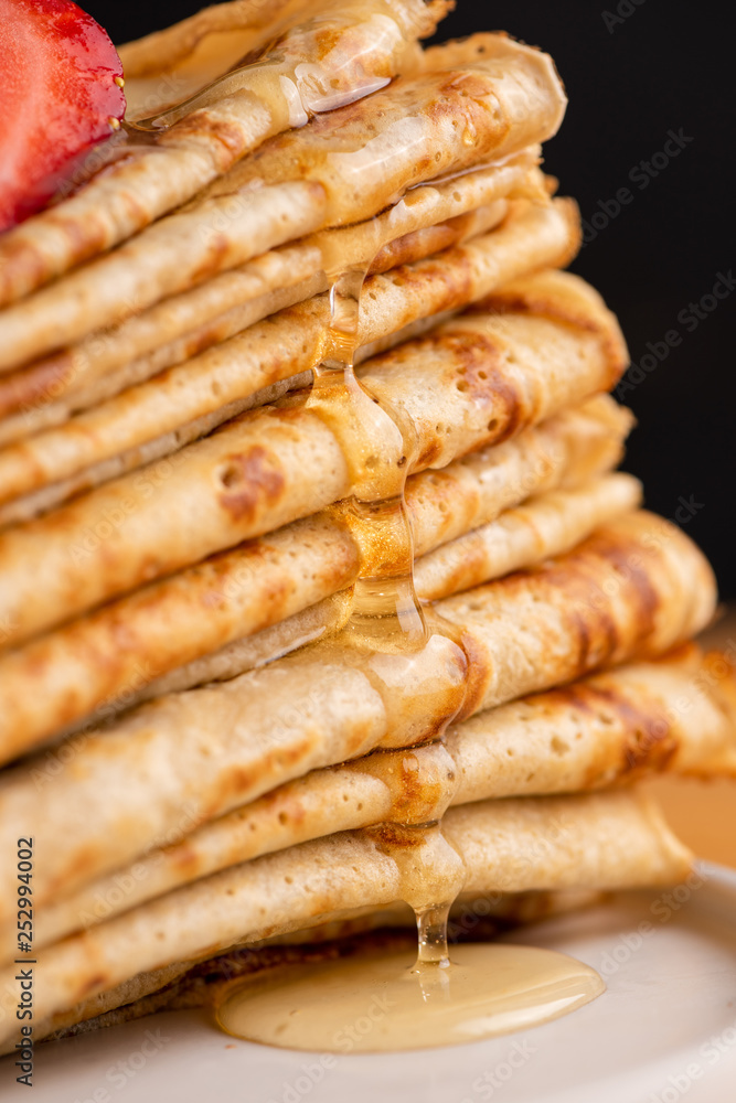 Honey or maple syrup pouring over crepes. Closeup view of stack of thin pancakes, blini or crepes with honey Honey or maple syrup pouring over crepes. Closeup view of stack of thin pancakes, blini or crepes with honey