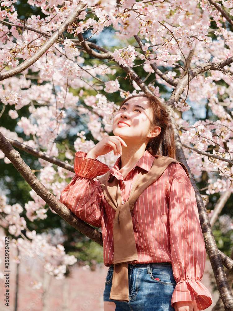 Outdoor portrait of beautiful young Chinese girl in red shirt posing among pink blossom cherry tree brunch in spring garden, beauty, summer, emotion, expression and people concept. Outdoor portrait of beautiful young Chinese girl in red shirt posing among pink blossom cherry tree brunch in spring garden, beauty, summer, emotion, expression and people concept.