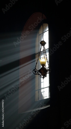 Piękne promienie światła wpadają przez duże wysokie okno kościoła, tworząc niezwykłą poświatę, piękna kuta lmpa zwisa z sufitu