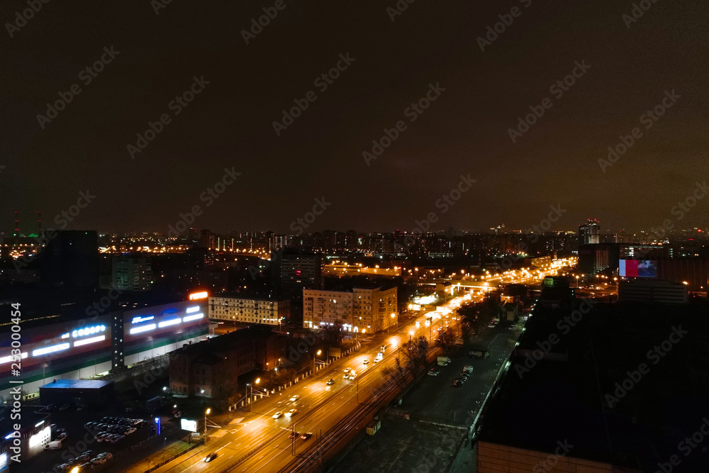 Aerial view of the night city. A wide motor road runs through the city block