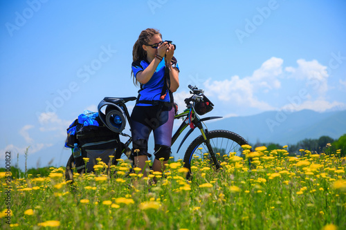 A girl with a bicycle shoots a photo on a flowered field
