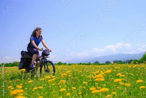 Girl tourist rides a bike among the flowering fields on the background of high mountains