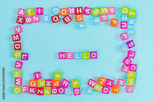 Hello inscription made of colorful cube beads with letters. Festive blue background concept with copy space.