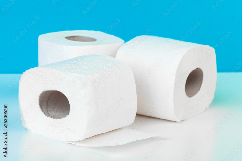 Three toilet paper rolls isolated on white table with blue background Three toilet paper rolls isolated on white table with blue background