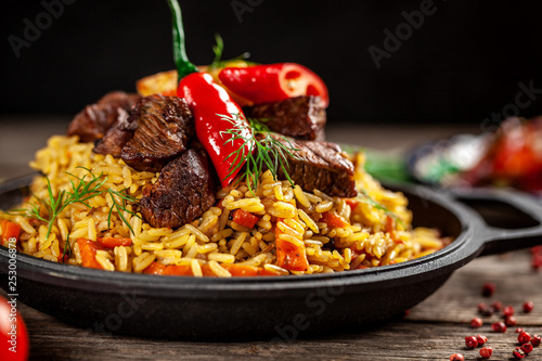 The concept of oriental cuisine. National Uzbek pilaf with meat in a cast-iron skillet, on a wooden table. background image. top view, copy space, flat lay