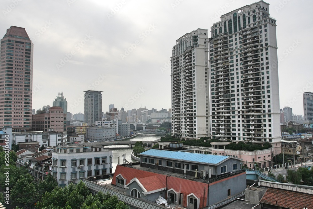 Cityscape in Shanghai China with skyscrapers, high rise and low rise buildings, and houses on cloudy, smoggy grey day