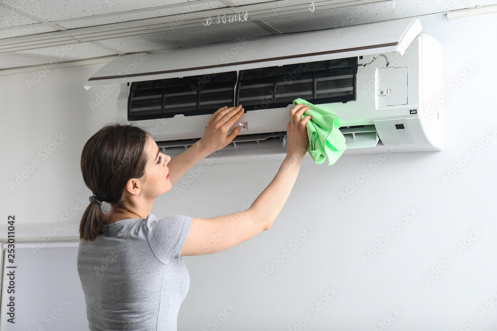 Young woman cleaning air conditioner at home Young woman cleaning air conditioner at home