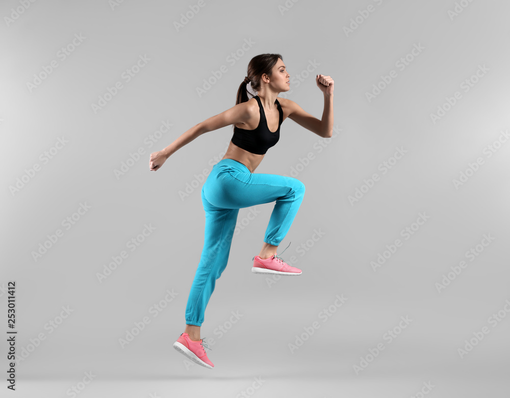 Sporty young woman jumping against light background