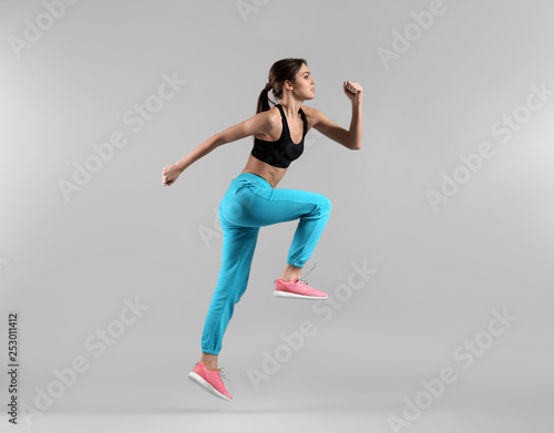 Sporty young woman jumping against light background