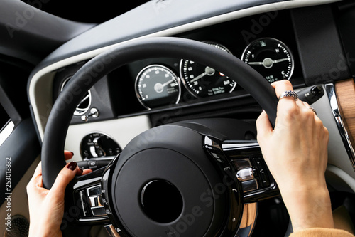 Woman's hands on the steering wheel driving modern luxury car. Concept woman driving. Hands holding steering wheel while driving. Car inside. Car detailing. © Aleksei