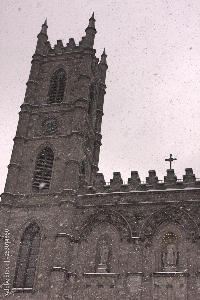 Stone cathedral tower in front of grey sky on snowy day