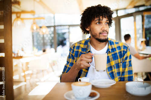 Starting new day in cafe. Side view of young african man holding coffee cup a