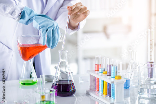 Scientist holding sampling oil or chemical liquid in flask with lab glassware in laboratory background, science or medical research and development concept