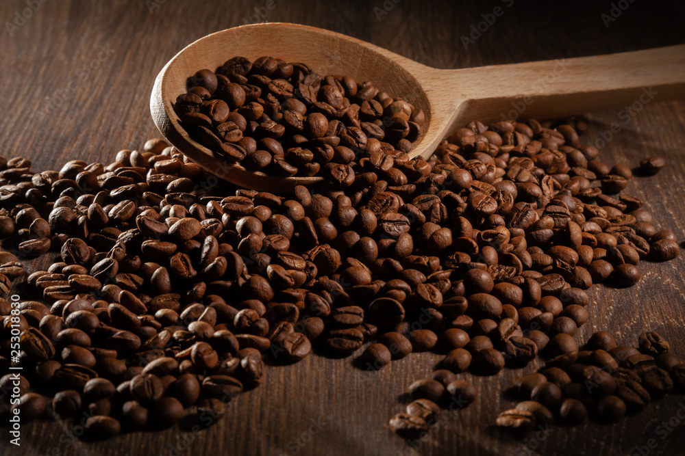 Naklejka premium Scattered coffee beans with wooden spoons on wooden table.