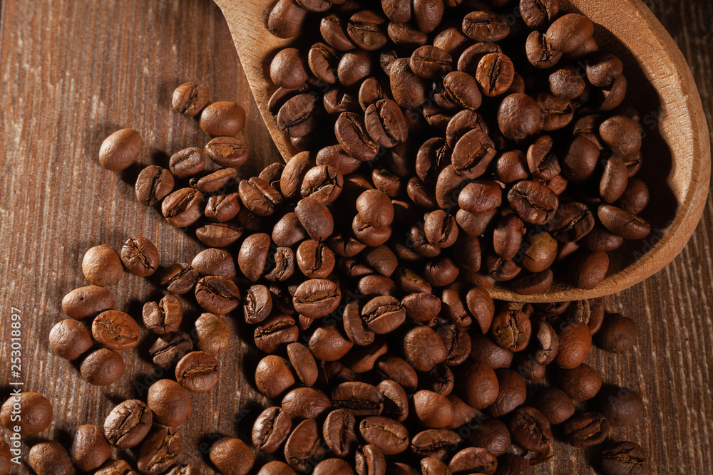 Scattered coffee beans with wooden spoons on wooden table. Scattered coffee beans with wooden spoons on wooden table.