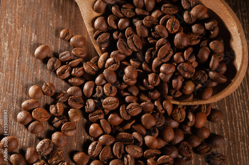  Scattered coffee beans with wooden spoons on wooden table.