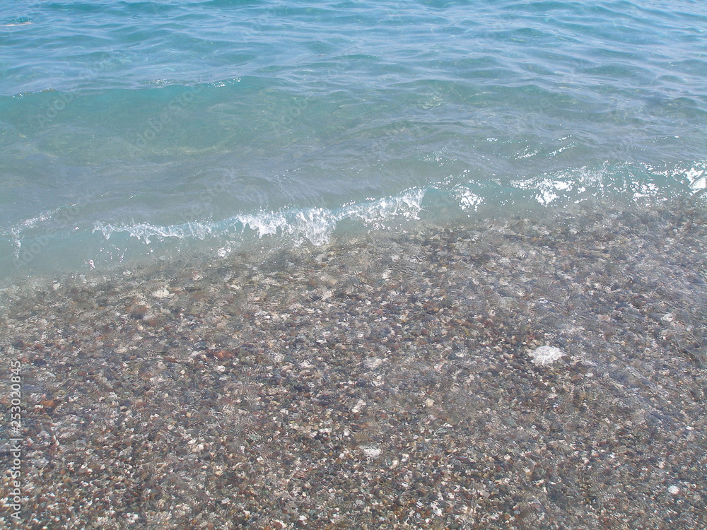 Sea wave runs on the beach covered with pebbles. Texture of clear turquoise water