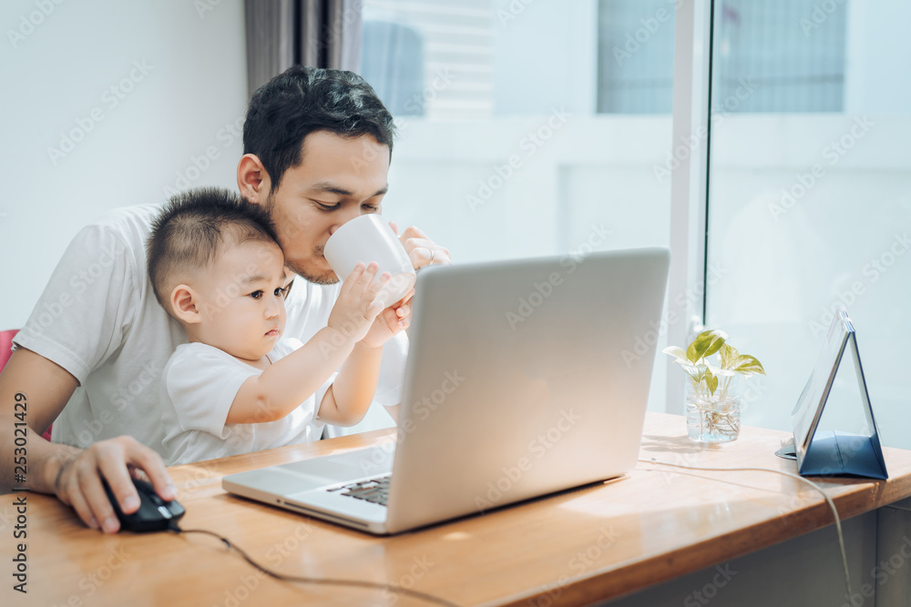 Asian little son helping father drinking coffee between working with laptop computer notebook at workplace happy family together at home concept. Asian little son helping father drinking coffee between working with laptop computer notebook at workplace happy family together at home concept.