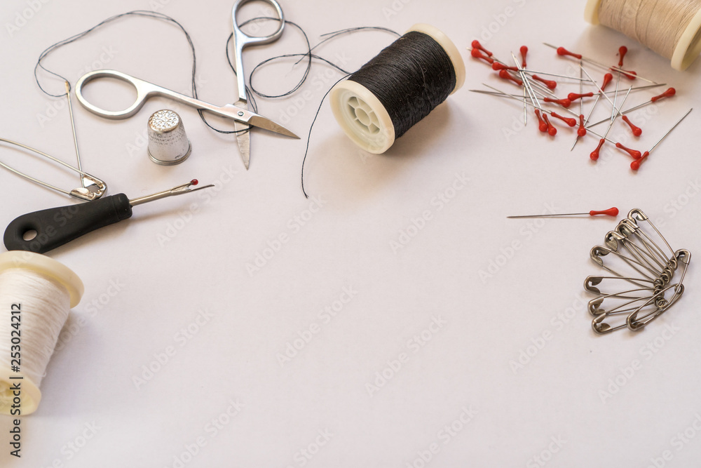 Selective focus on a black thread spool next to various accessories for fixing and repairing clothes, on a white background with copy space. Quick fix sewing kit. Tailor and craft concept. Selective focus on a black thread spool next to various accessories for fixing and repairing clothes, on a white background with copy space. Quick fix sewing kit. Tailor and craft concept.