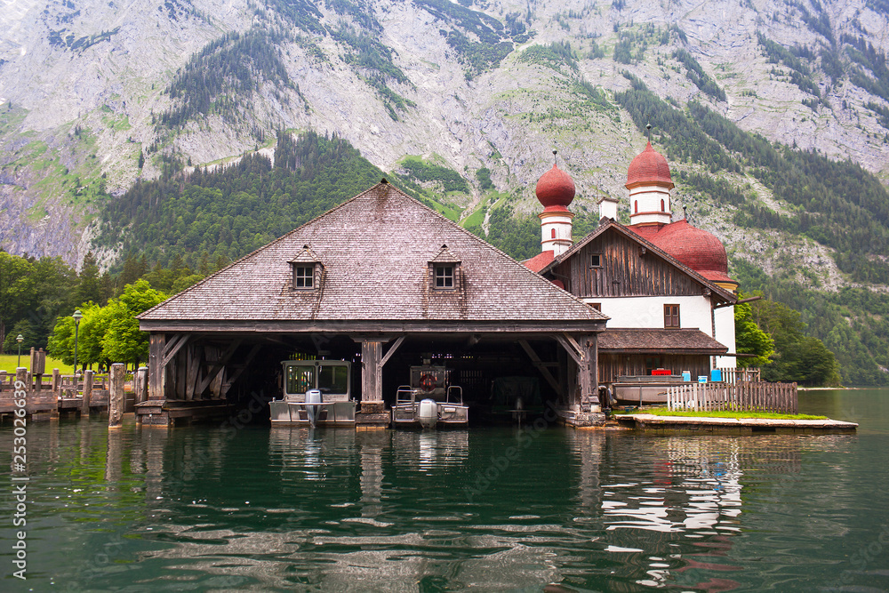 Naklejka premium Wooden dock for boats with a temple and mountains in the background on Konigssee Lake, Austria