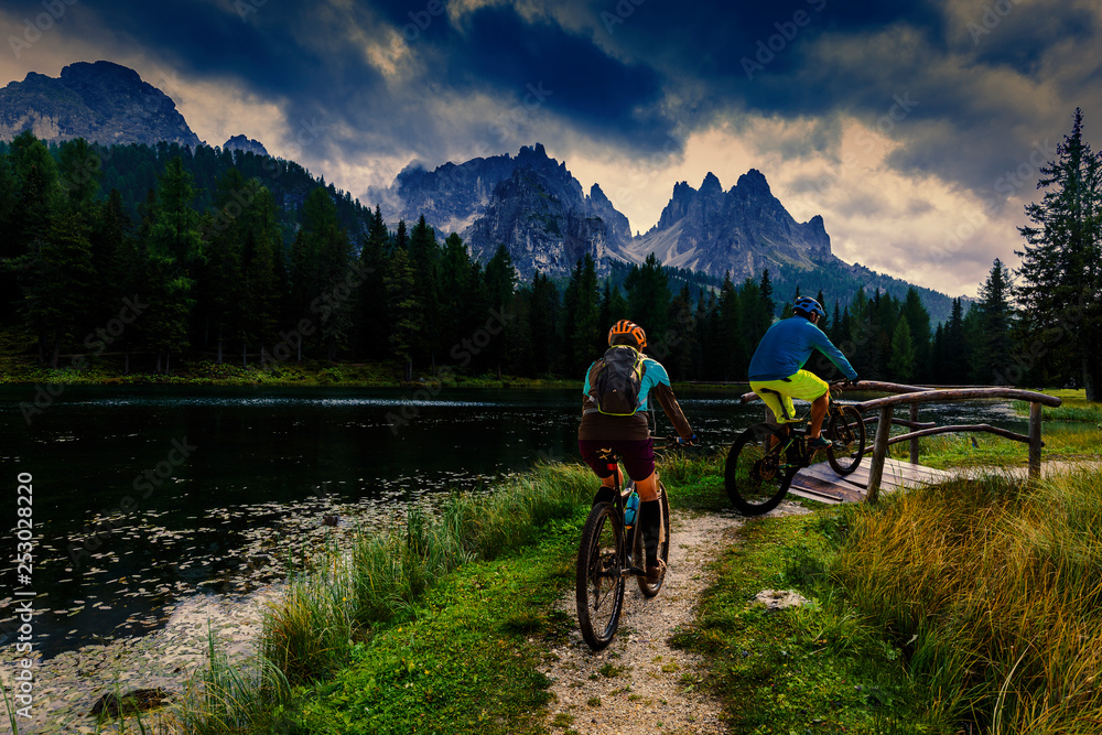 Fototapeta premium Cycling woman and man riding on bikes in Dolomites mountains andscape. Couple cycling MTB enduro trail track. Outdoor sport activity.