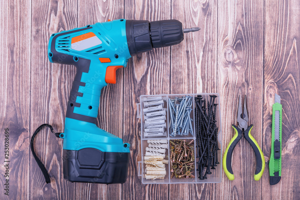 Modern rechargeable screwdriver, set of screws and tools on wooden background Modern rechargeable screwdriver, set of screws and tools on wooden background