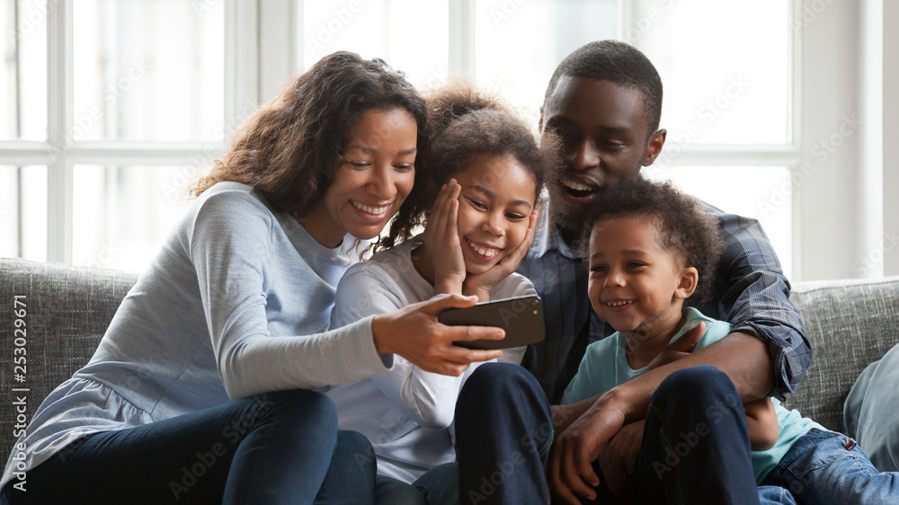 Smiling black family relax together watching cartoons on smartphone Smiling black family relax together watching cartoons on smartphone