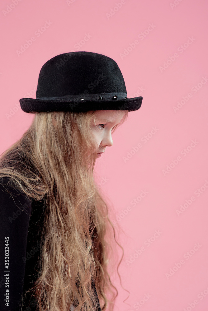 funny cute serious little girl with long blonde hair in black blazer and stylish black hat on pink background funny cute serious little girl with long blonde hair in black blazer and stylish black hat on pink background