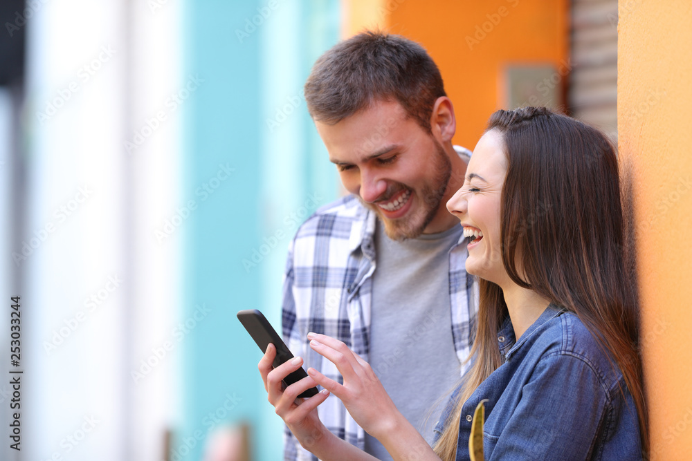 Happy couple laughing checking smart phone Happy couple laughing checking smart phone