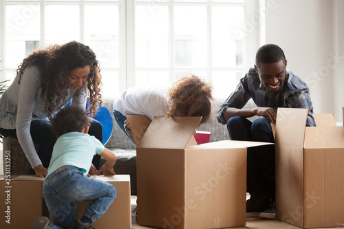 Happy black family with small kids unpack boxes