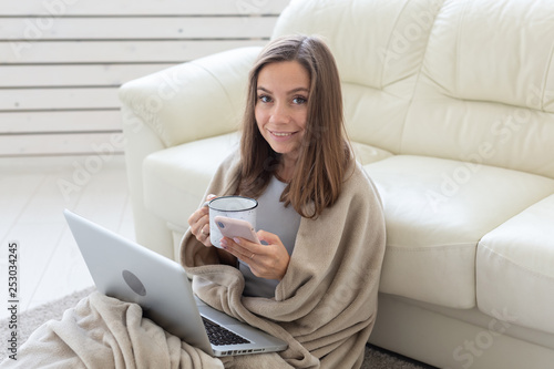 Working, cozy, people concept - young woman working at home in plaid, drinking tea and chatting in netbook