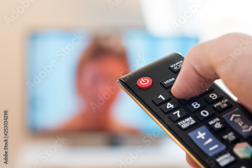 tv remote control in a hand of a person with a television in the background