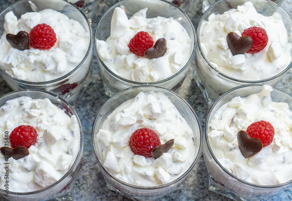 Fresh cream desserts in glasses with crumbles, a chocolate heart and one raspberry Fresh cream desserts in glasses with crumbles, a chocolate heart and one raspberry